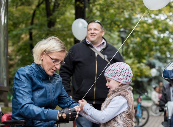 Мама-инвалид привязывает дочке на руку воздушный шарик, чтобы он не улетел